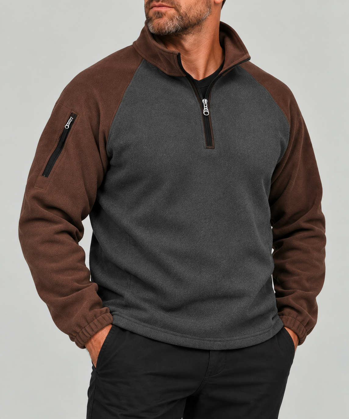 A man wearing a brown and dark gray quarter-zip fleece pullover sweatshirt with a zippered sleeve pocket, shown from the chin down against a light gray studio background.
